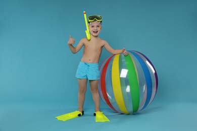 Photo of Cute little boy in beachwear with snorkeling equipment and inflatable ball showing thumbs up on light blue background