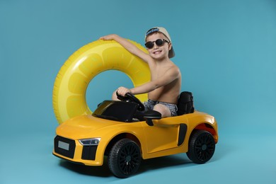 Photo of Cute little boy in beachwear with inflatable ring and toy car on light blue background