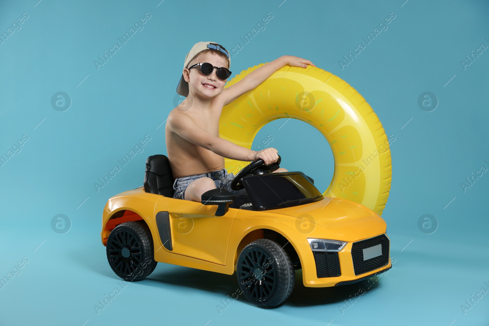 Photo of Cute little boy in beachwear with inflatable ring and toy car on light blue background