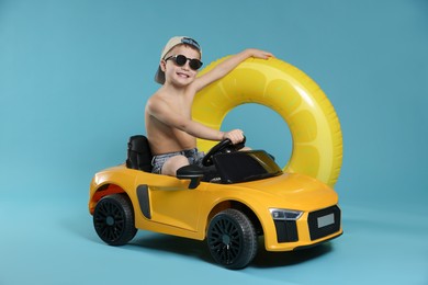 Photo of Cute little boy in beachwear with inflatable ring and toy car on light blue background