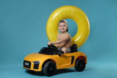 Photo of Cute little boy in beachwear with inflatable ring and toy car on light blue background