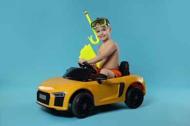 Photo of Cute little boy in beachwear with snorkeling equipment and toy car on light blue background