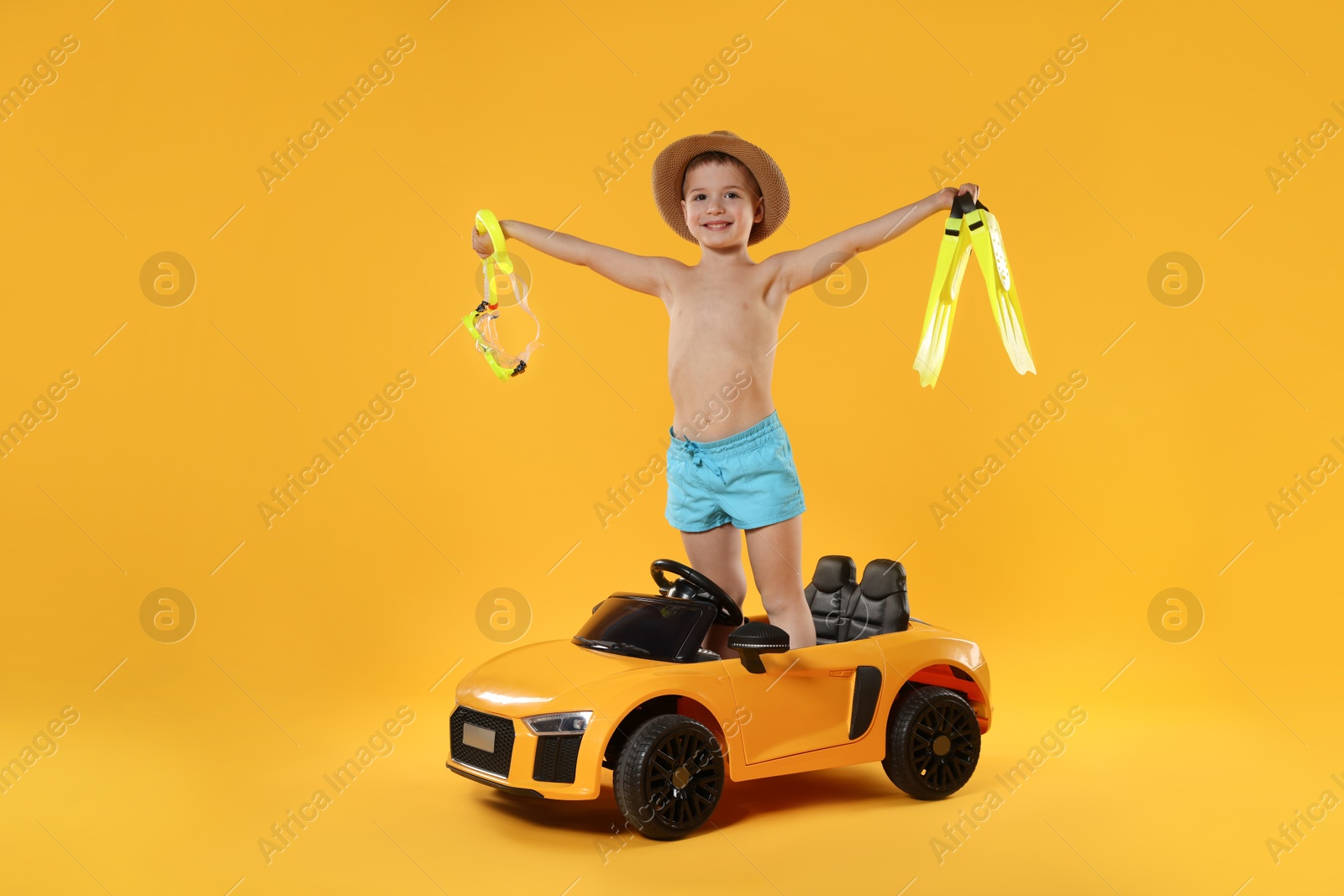 Photo of Cute little boy in beachwear with snorkeling equipment and toy car on orange background