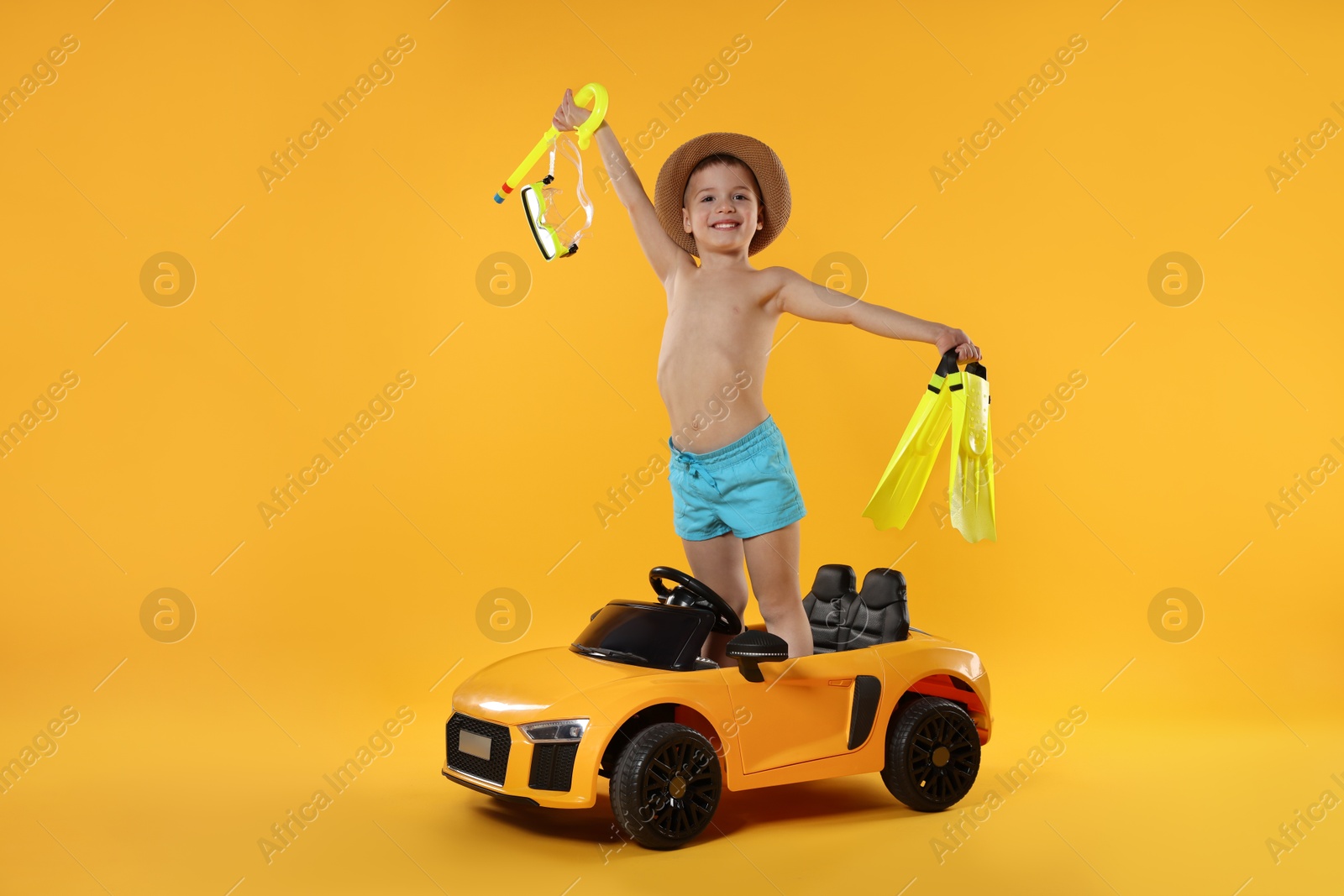 Photo of Cute little boy in beachwear with snorkeling equipment and toy car on orange background