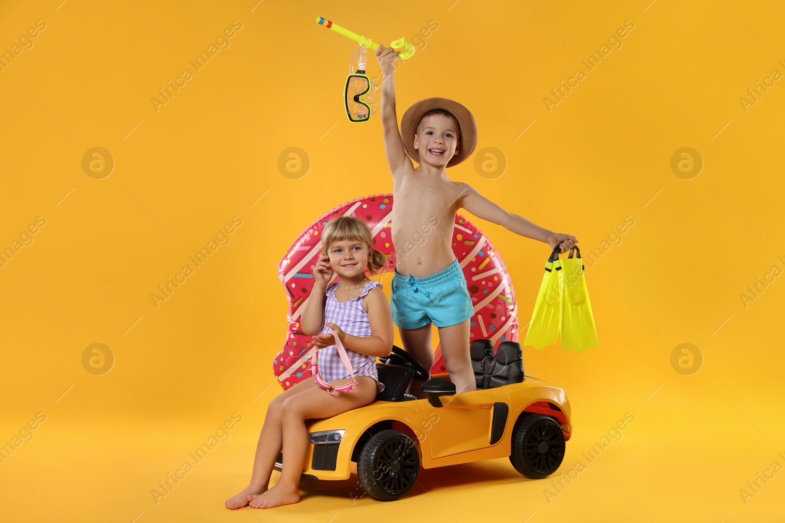 Photo of Cute little kids in beachwear with inflatable ring and toy car on orange background