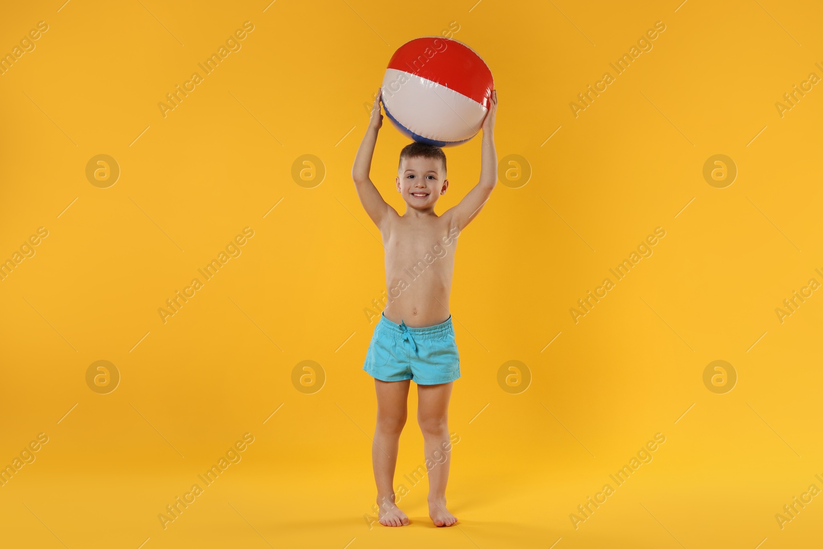 Photo of Cute little boy in beachwear with inflatable ball on orange background