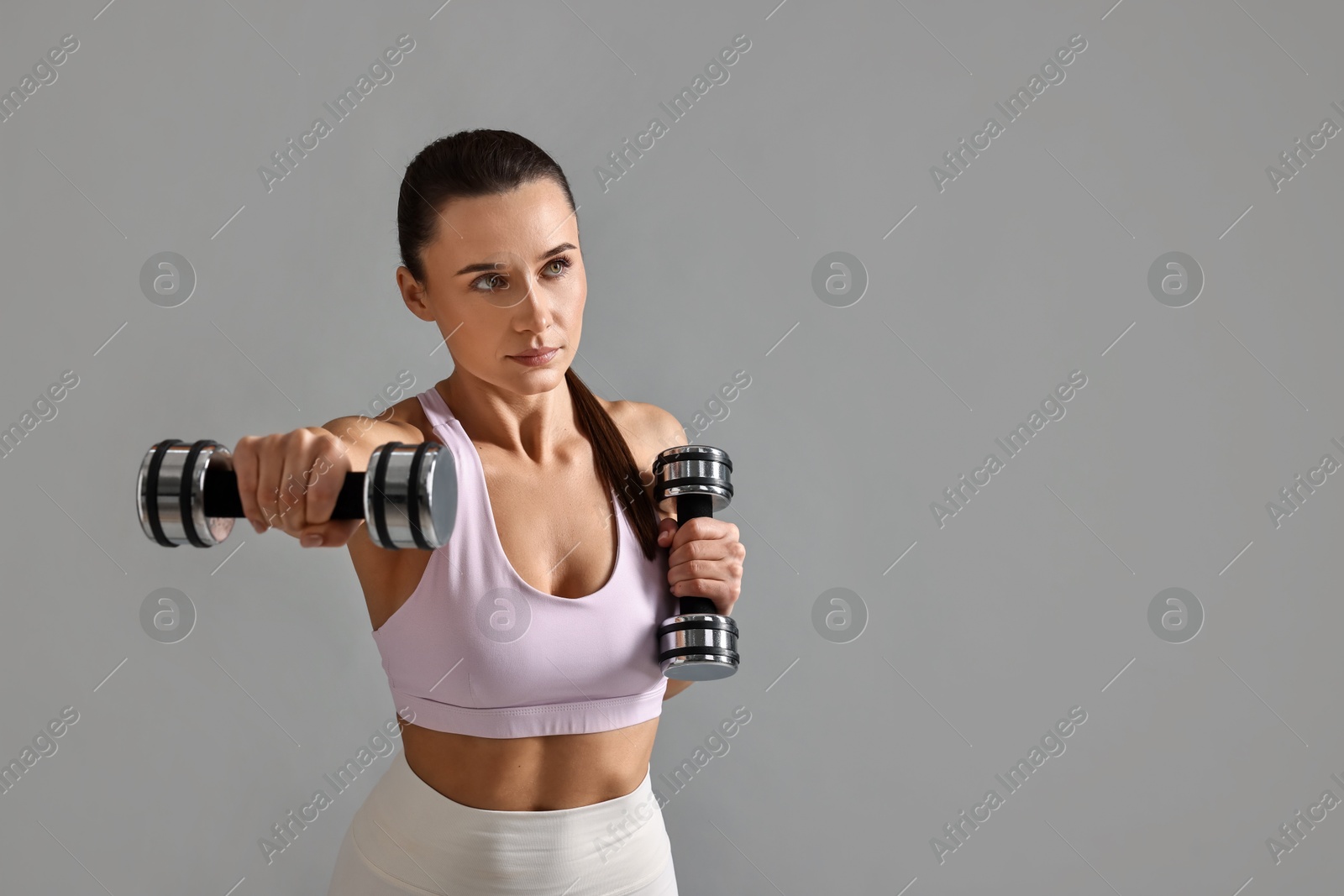 Photo of Woman in gym clothes exercising with dumbbells on grey background, space for text