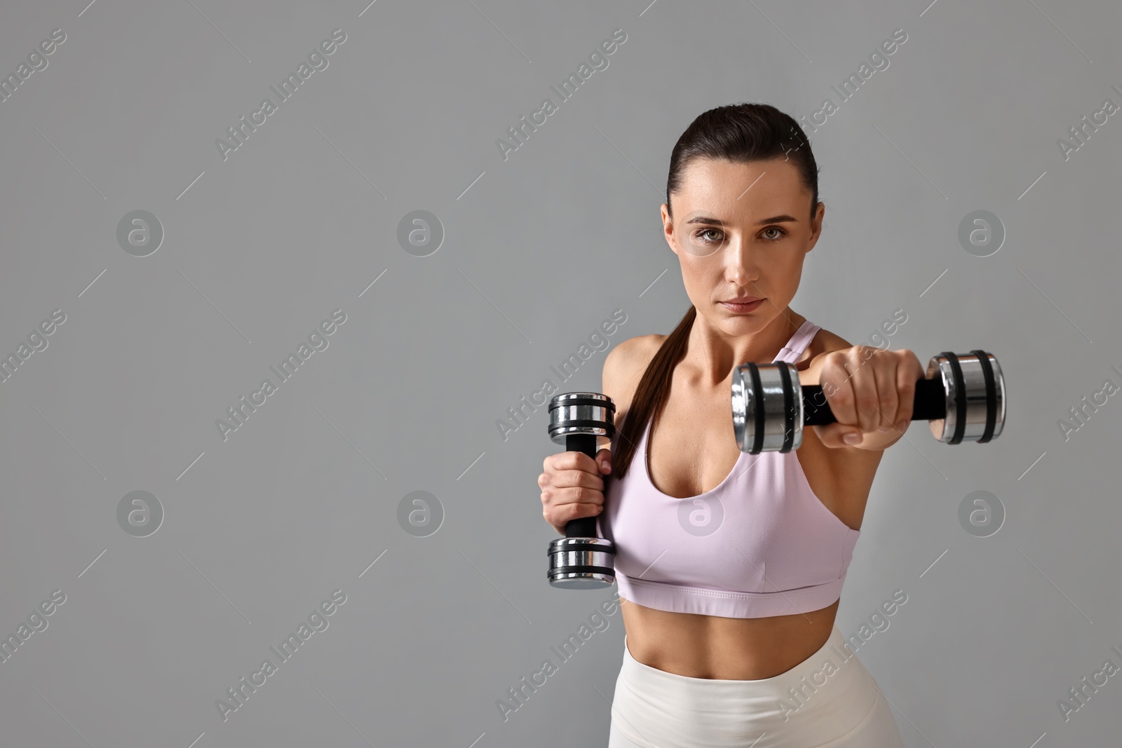 Photo of Woman in gym clothes exercising with dumbbells on grey background, space for text