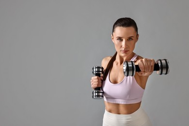 Photo of Woman in gym clothes exercising with dumbbells on grey background, space for text