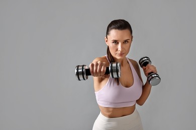 Photo of Woman in gym clothes exercising with dumbbells on grey background, space for text