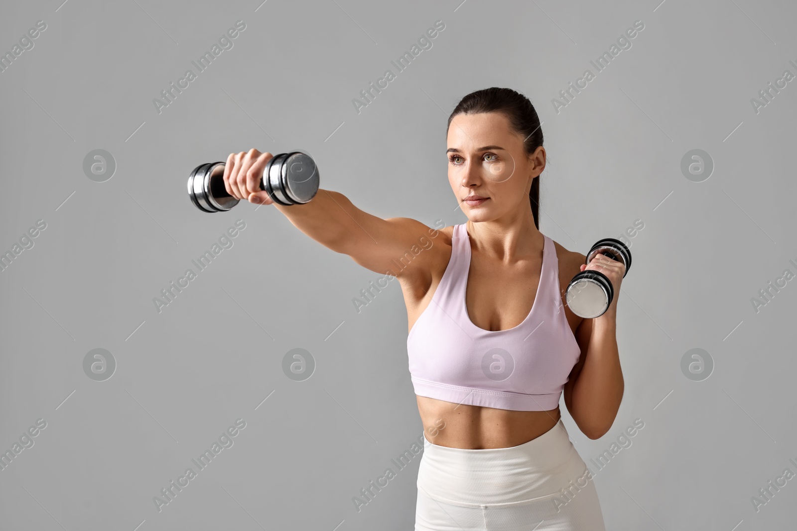 Photo of Woman in gym clothes exercising with dumbbells on grey background