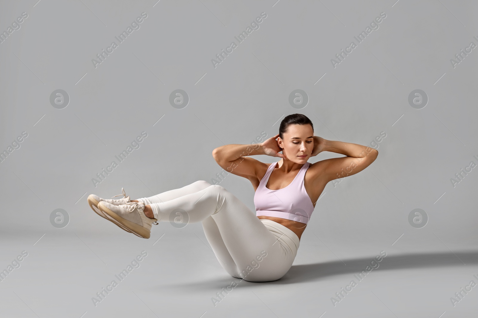 Photo of Woman in gym clothes doing abs exercise on grey background