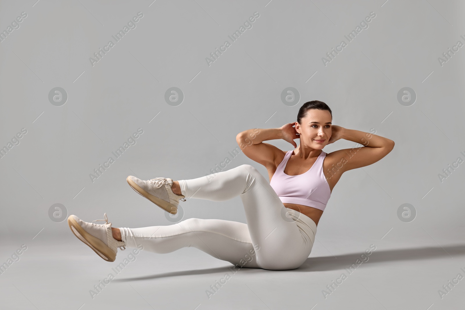 Photo of Woman in gym clothes doing abs exercise on grey background