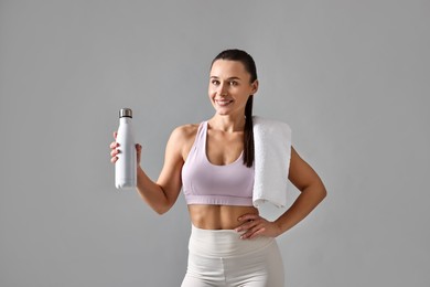 Photo of Woman in gym clothes with thermo bottle and towel on grey background