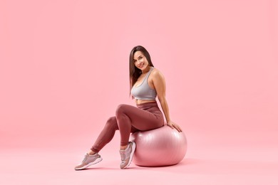 Photo of Woman in gym clothes with fitness ball on pink background