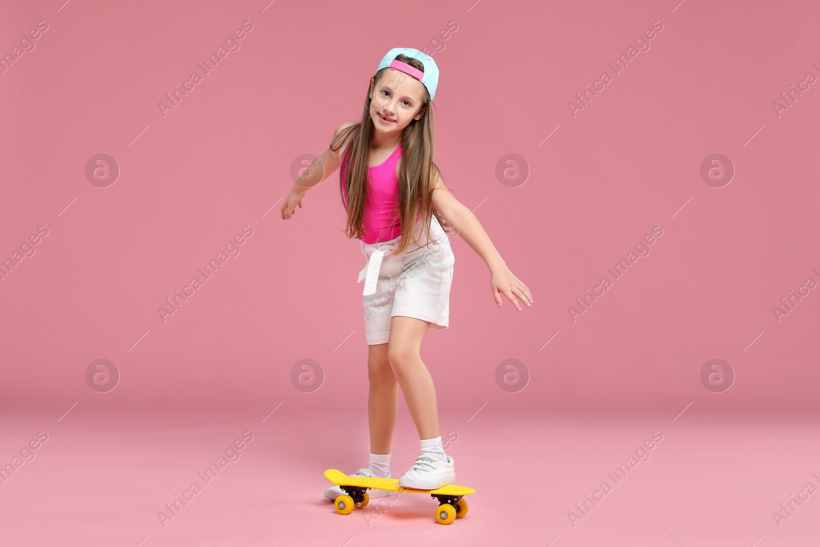 Photo of Little girl with penny board on pink background