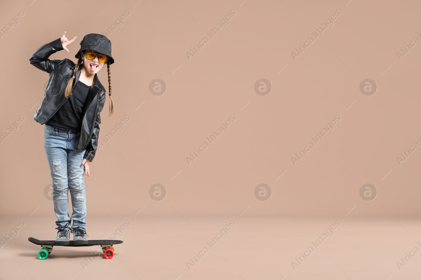 Photo of Little girl standing on penny board against pale brown background, space for text