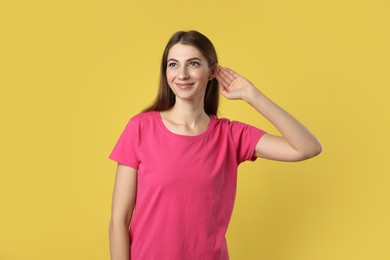 Photo of Woman showing hand to ear gesture on dark yellow background