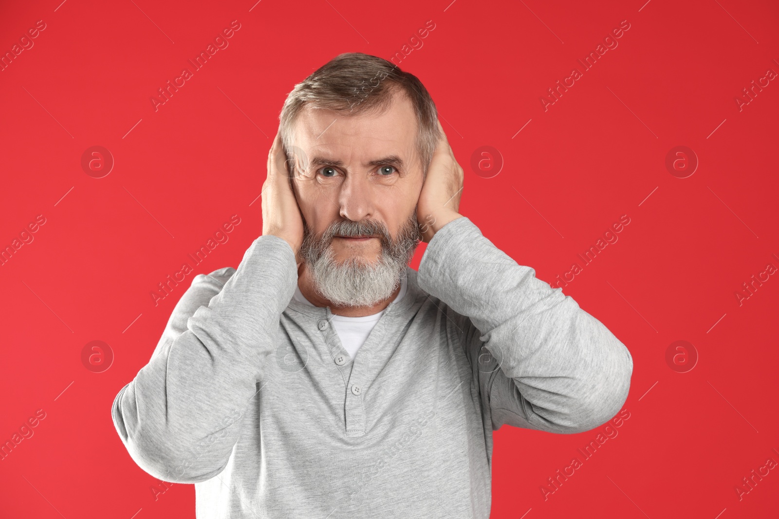 Photo of Senior man covering his ears on red background