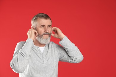 Photo of Senior man covering his ears with fingers on red background. Space for text