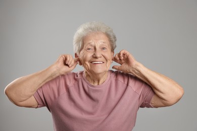 Photo of Senior woman covering her ears with fingers on grey background