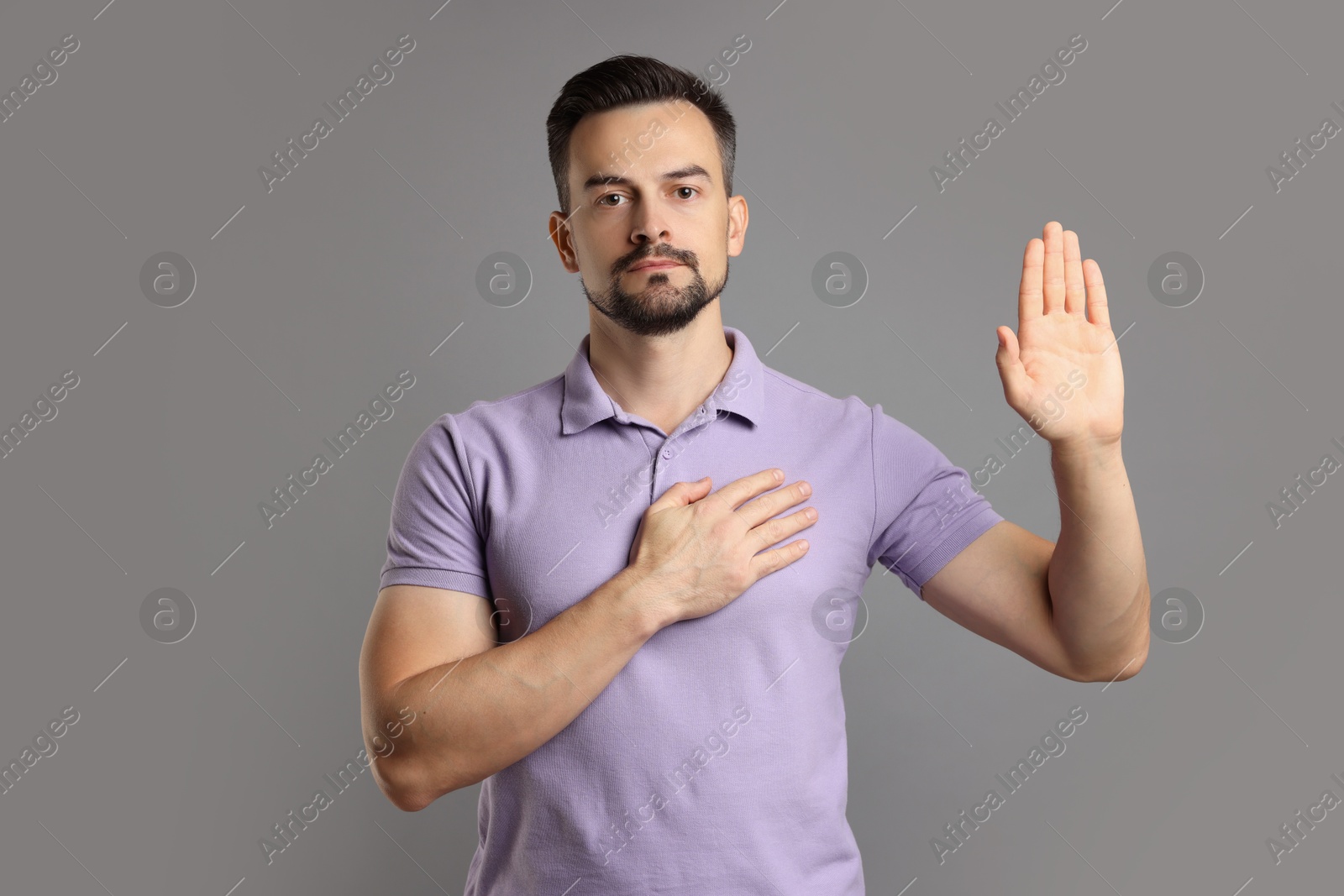 Photo of Man making promise with raised hand on grey background. Oath gesture