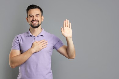 Photo of Man making promise with raised hand on grey background, space for text. Oath gesture