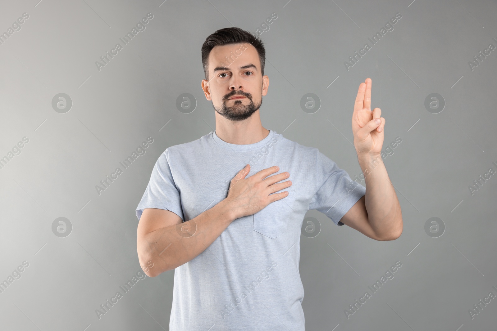 Photo of Man showing oath gesture on grey background. Making promise