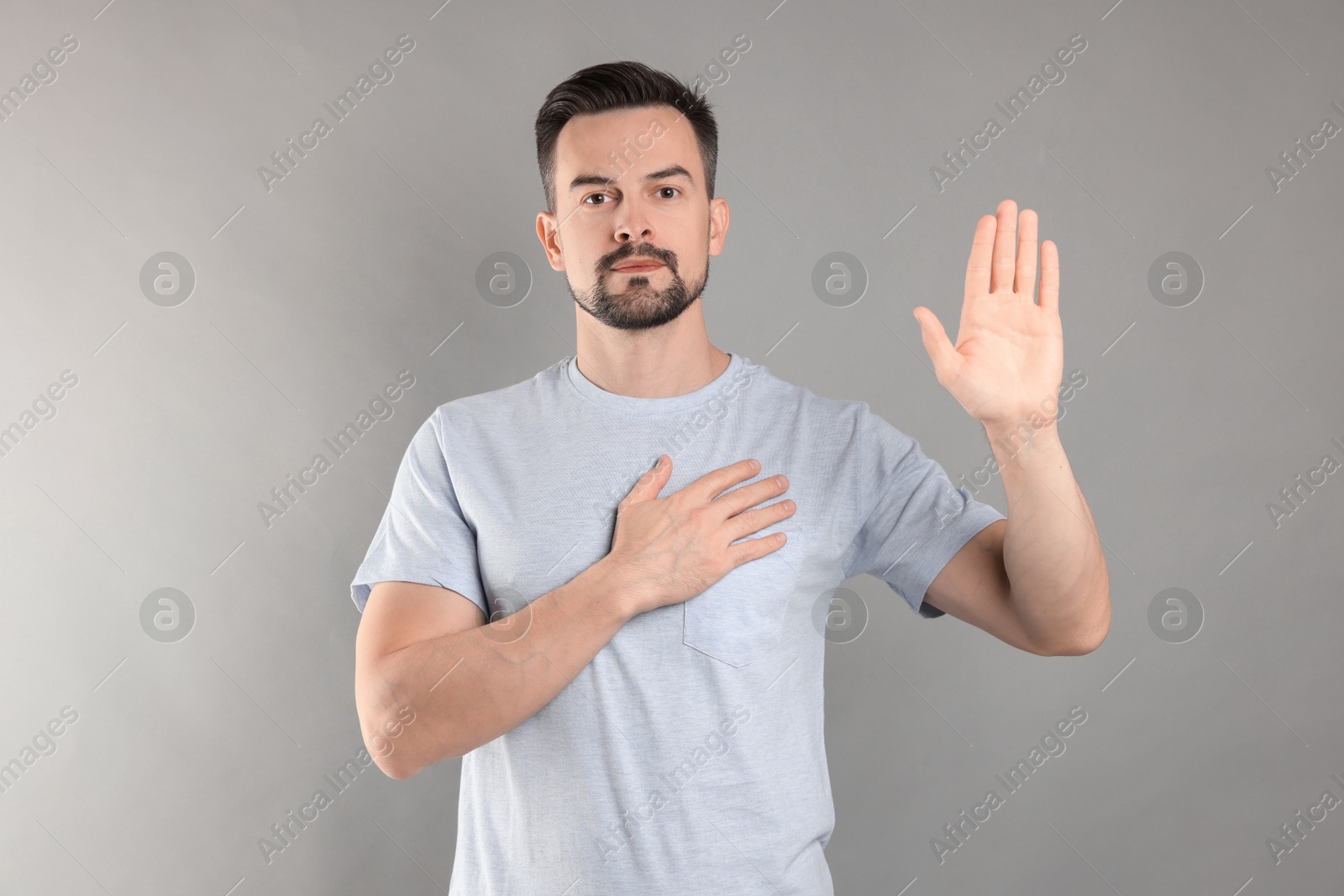 Photo of Man making promise with raised hand on grey background. Oath gesture