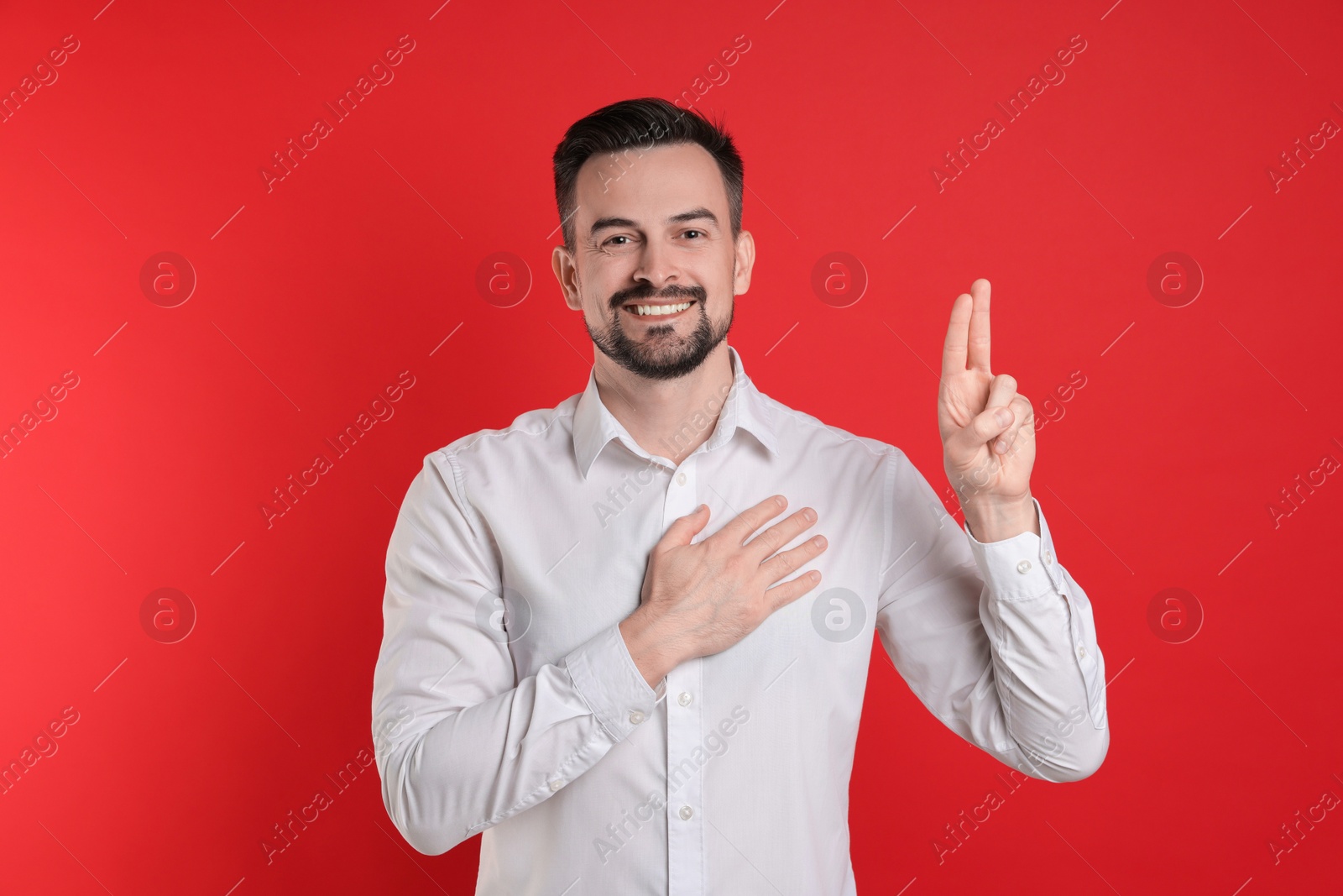 Photo of Man showing oath gesture on red background. Making promise