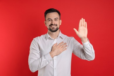 Photo of Man making promise with raised hand on red background. Oath gesture