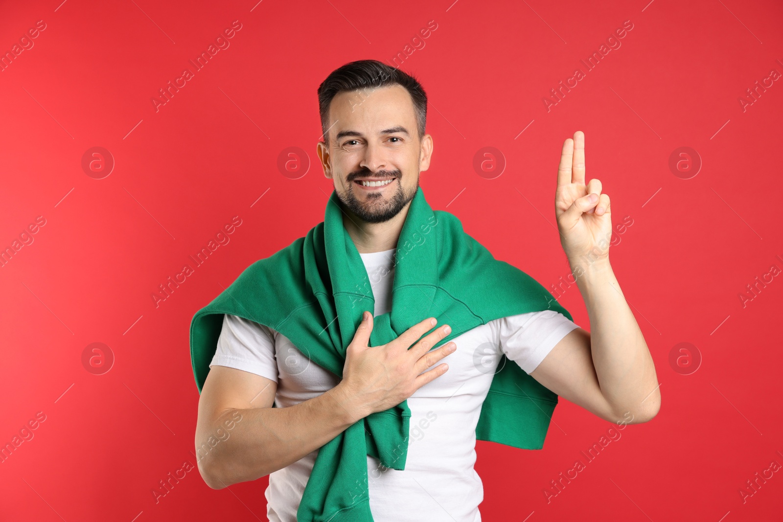 Photo of Man showing oath gesture on red background. Making promise