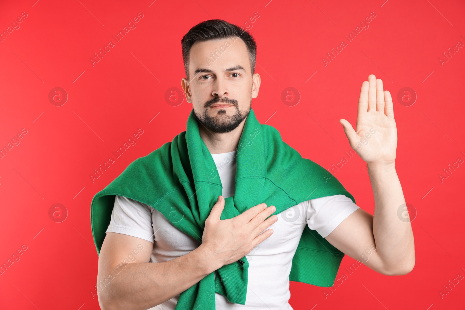 Photo of Man making promise with raised hand on red background. Oath gesture