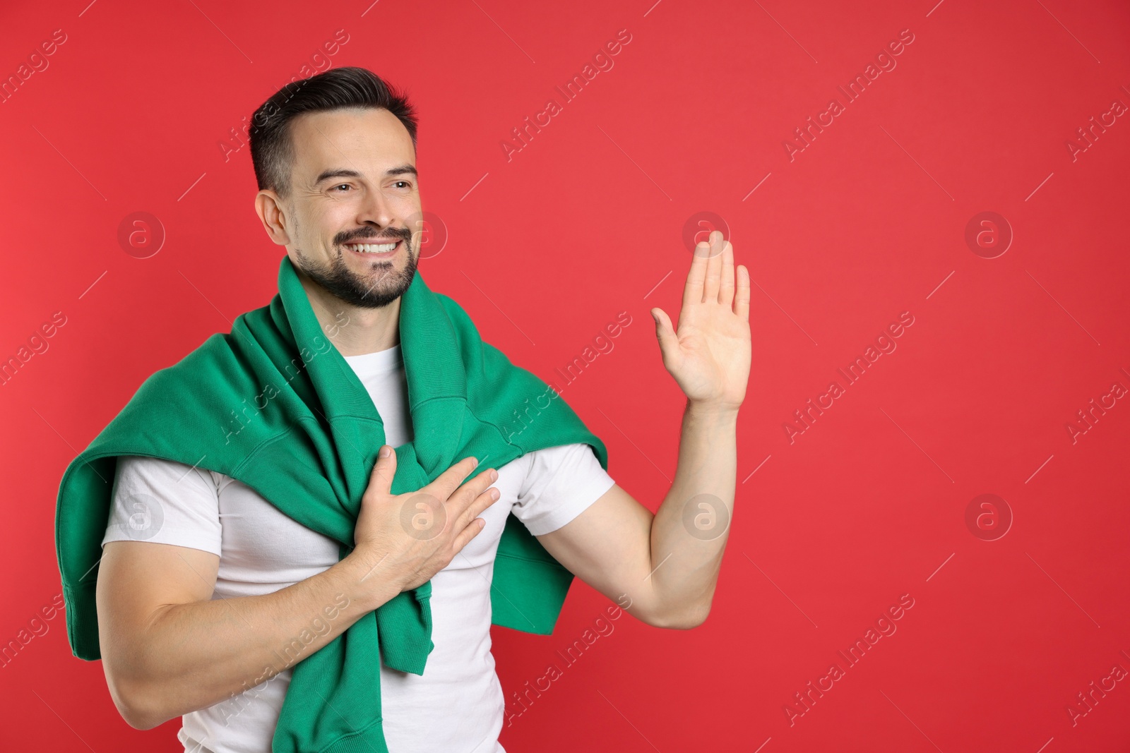 Photo of Man making promise with raised hand on red background, space for text. Oath gesture