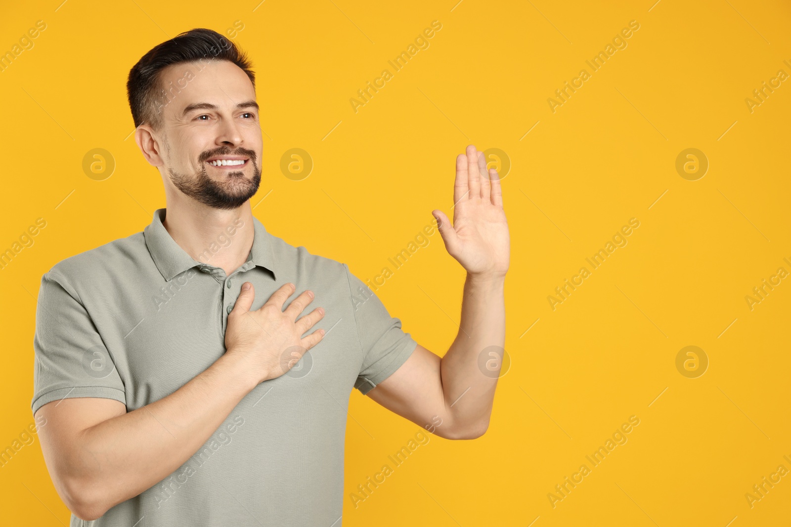 Photo of Man making promise with raised hand on orange background, space for text. Oath gesture