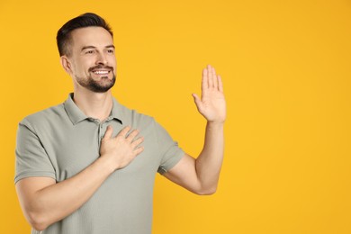 Photo of Man making promise with raised hand on orange background, space for text. Oath gesture