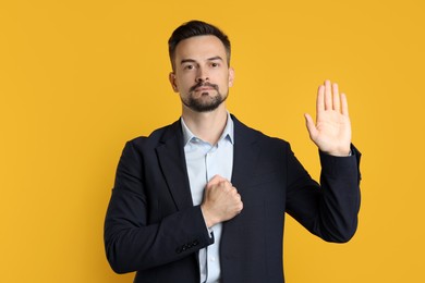 Photo of Man making promise with raised hand on orange background. Oath gesture