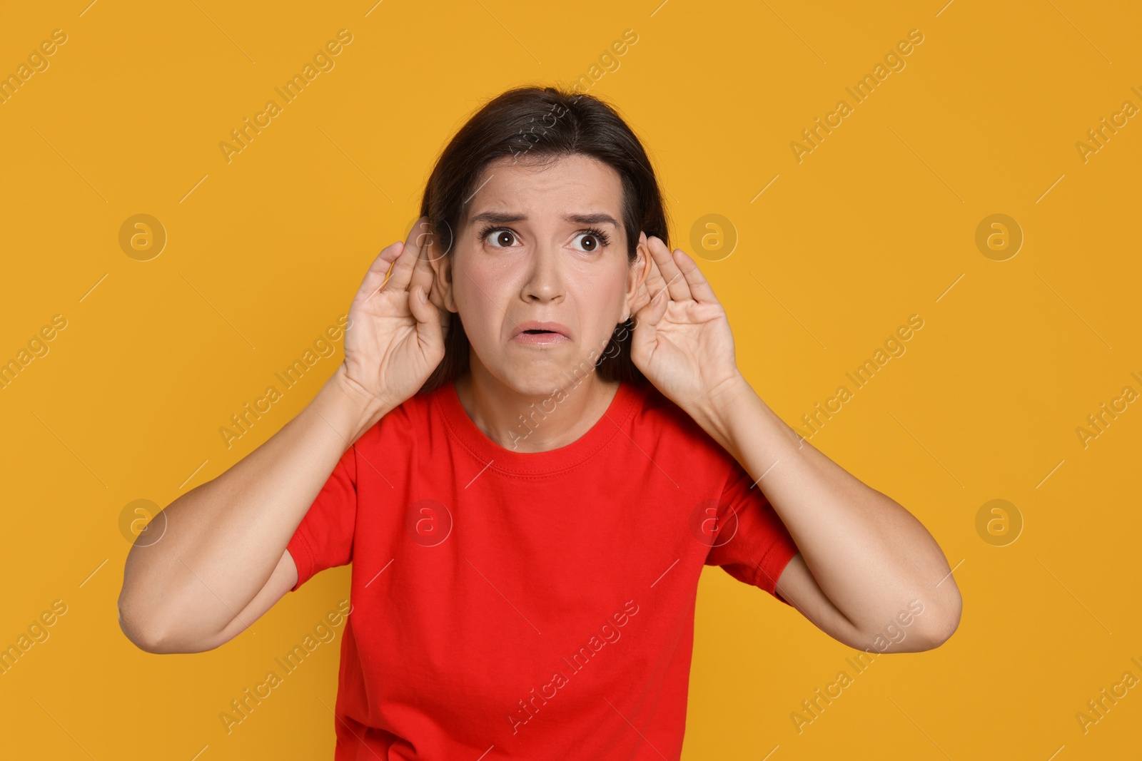 Photo of Woman showing hand to ear gesture on orange background