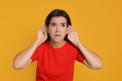 Photo of Woman showing hand to ear gesture on orange background