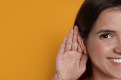 Photo of Woman showing hand to ear gesture on orange background, closeup. Space for text