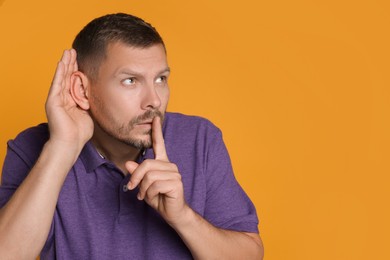 Photo of Man showing hand to ear gesture on orange background, space for text