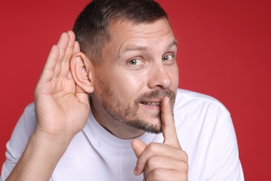 Photo of Man showing hand to ear gesture on red background