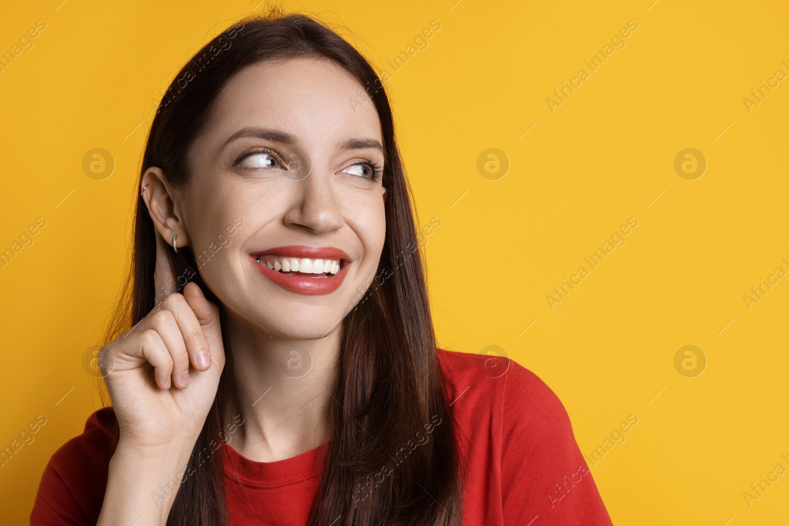 Photo of Woman showing hand to ear gesture on orange background. Space for text