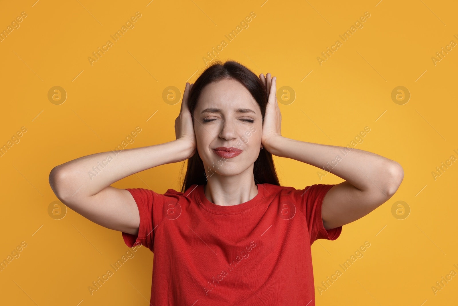 Photo of Woman covering her ears on orange background