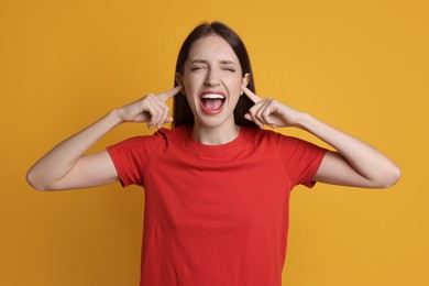 Photo of Woman covering her ears with fingers on orange background