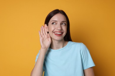 Photo of Woman showing hand to ear gesture on orange background