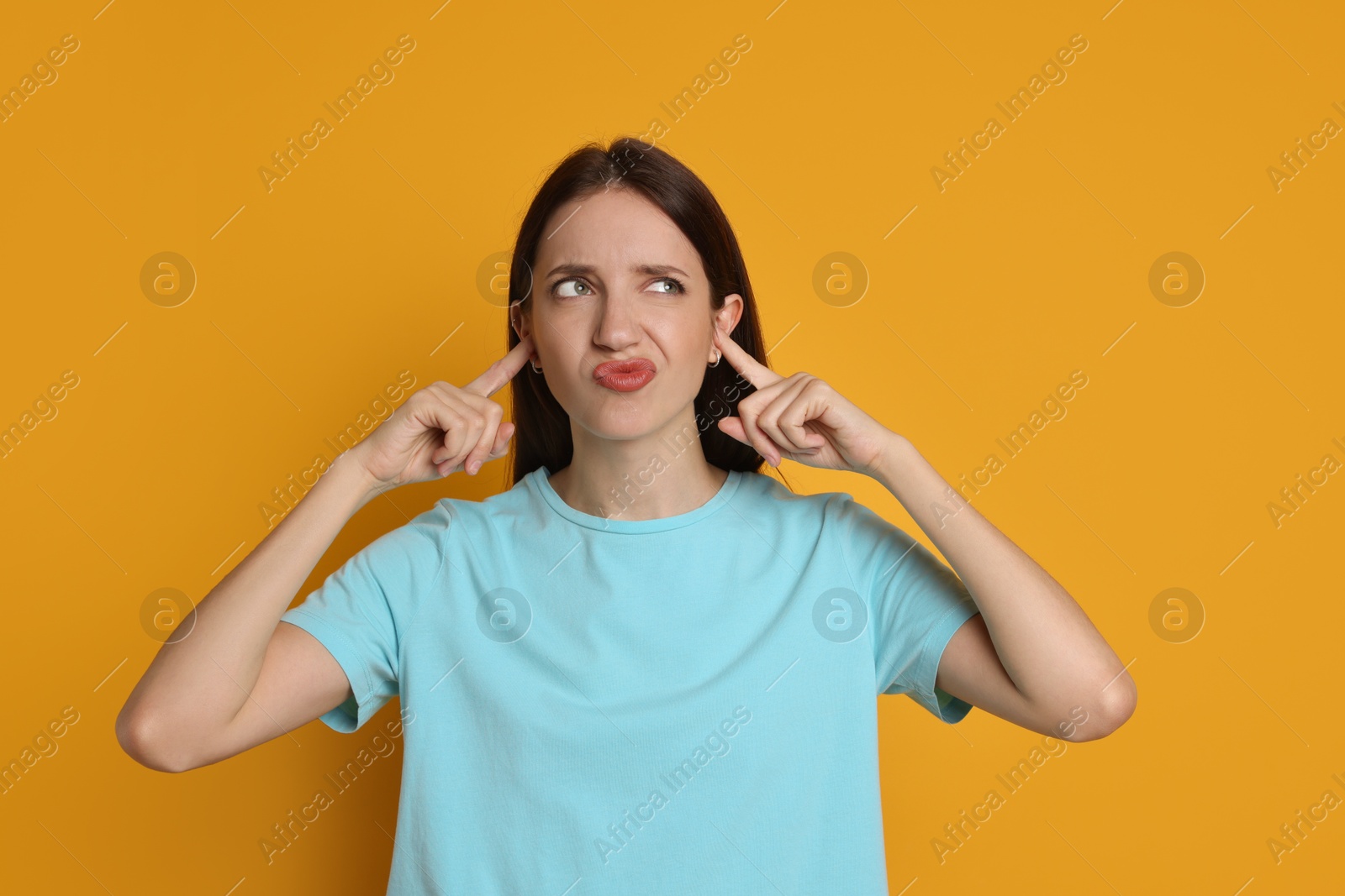 Photo of Woman covering her ears with fingers on orange background