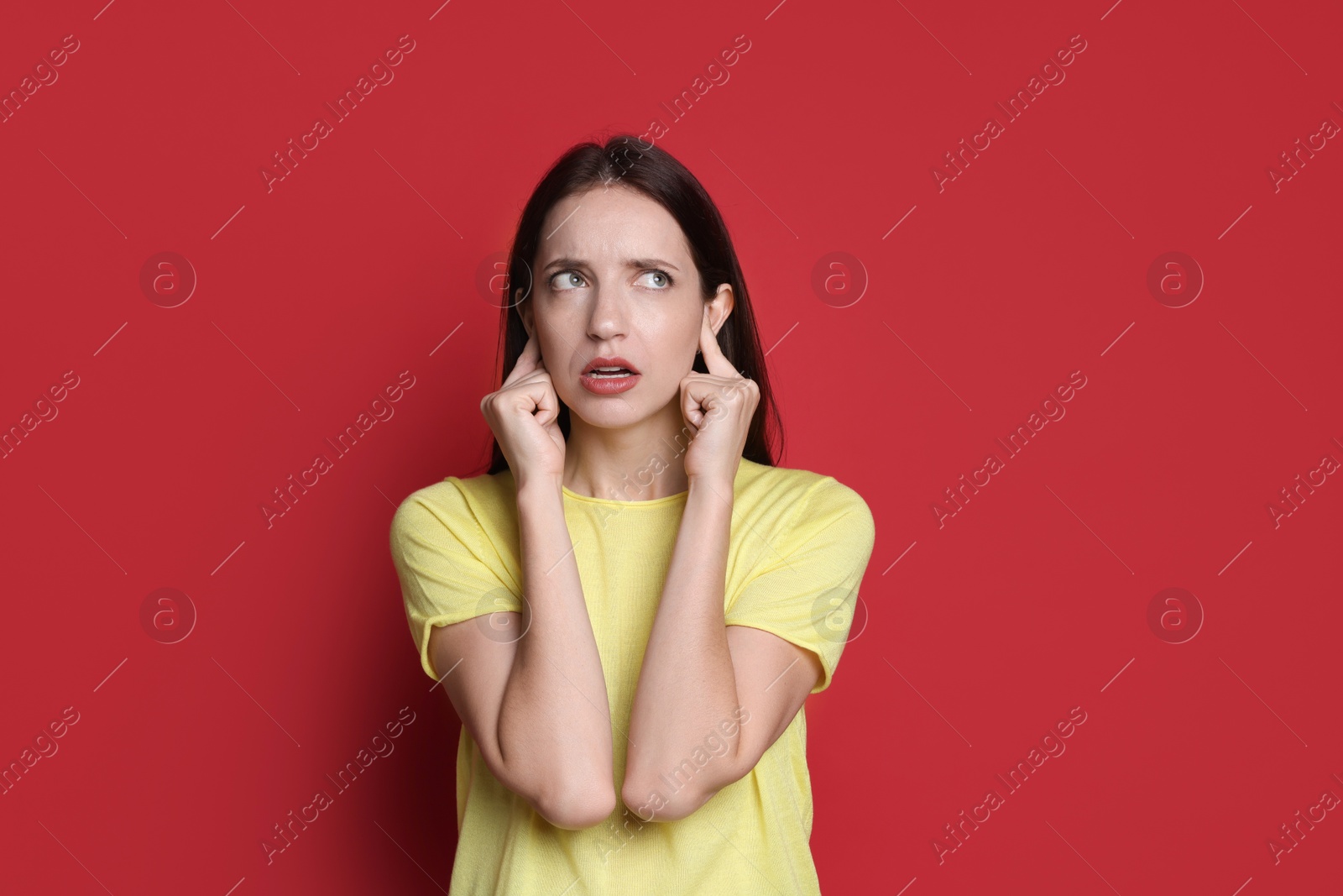 Photo of Woman covering her ears with fingers on red background