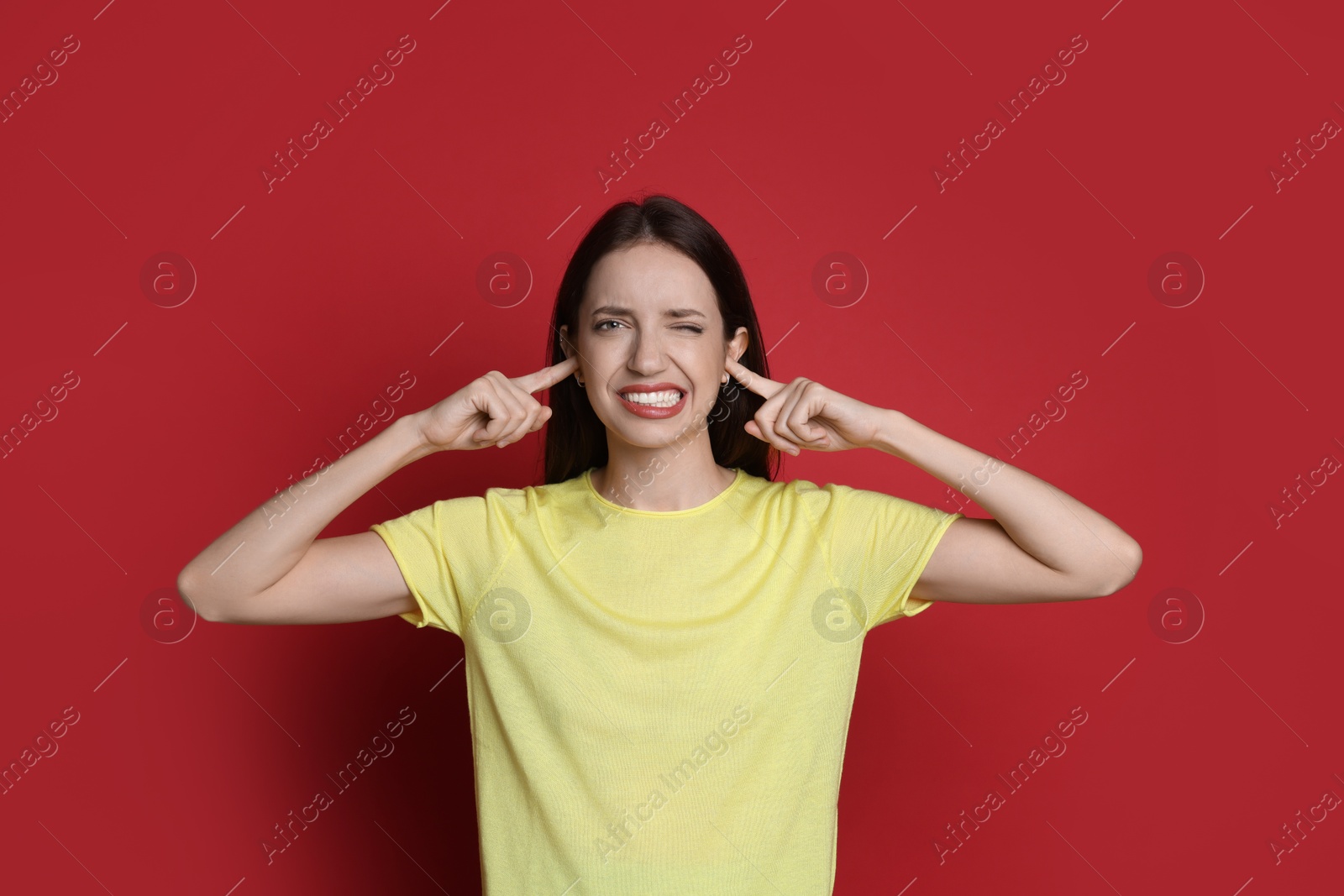 Photo of Woman covering her ears with fingers on red background