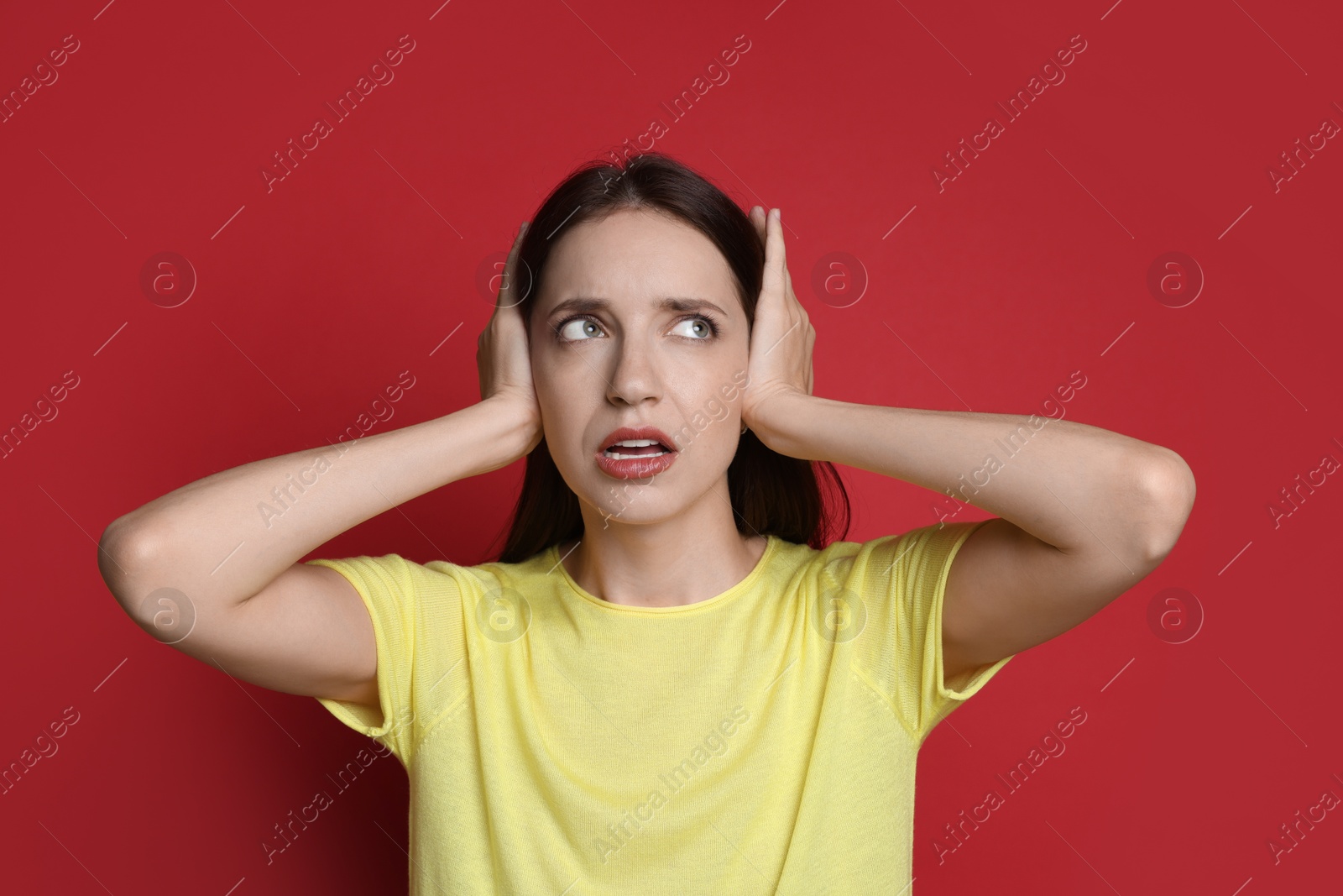 Photo of Woman covering her ears on red background